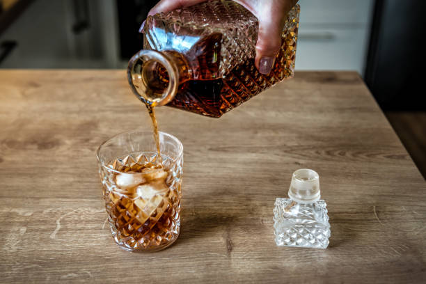 whisky wird in ein aufgestautes glas mit natureis gegossen. glas whisky auf einem eichentisch. - wine decanter elegance pouring stock-fotos und bilder