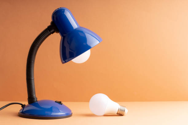istock replacing a light bulb in a table lamp, one light bulb in the lamp another on the table 1432289623