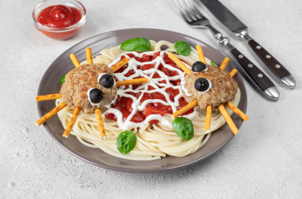 istock Cutlets look like spiders with olive eyes and straws, served with spaghetti pasta and tomato sauce on gray background. Halloween breakfast 1432289708