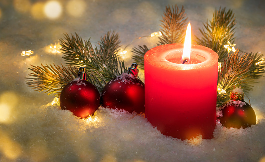 closeup of a christmas decoration with red shiny candlelight with balls and fir tree branches in snow, merry christmas greeting card