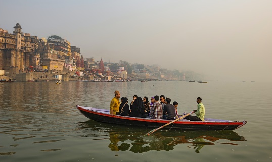 Varanasi, India, November 23, 2015: A group of tourists sails on a boat on the Ganges River in this foggy town at sunrise. Varanasi is the central place in pilgrimage, death, and mourning in the Hindu world.