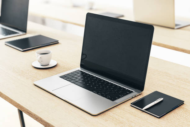 istock Perspective view on modern laptop with blank dark screen with copyspace for your website page on wooden table with coffee cup, black notebook with pen on blurry office background. 3D rendering, mockup 1432293106