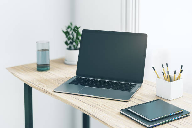 istock Perspective view on blank dark modern laptop monitor with copyspace for your logo or text on wooden table with glass of water and notebooks in light walls sunny room. 3D rendering, mockup 1432294526