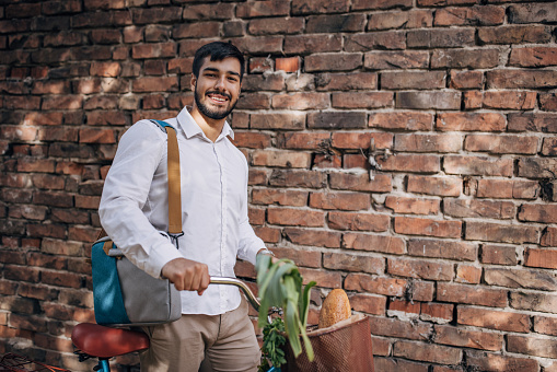 One man, modern young businessman pushing his bicycle with groceries after work in city.