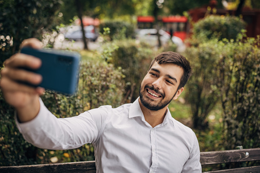One man, modern businessman sitting on park bench, he is talking a selfie with mobile phone.