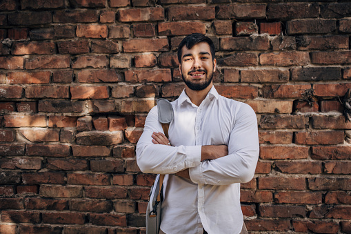 One man, portrait of a modern young businessman standing by a brick wall.