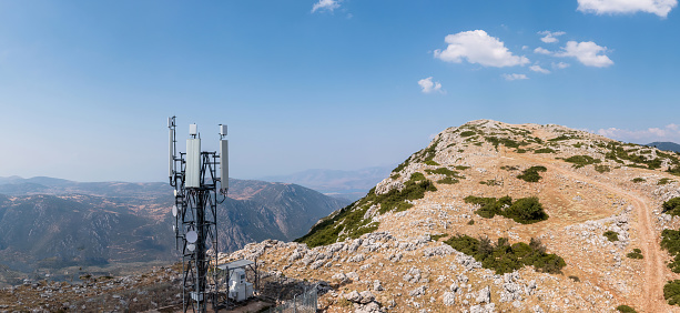 Cell phone tower. Mobile 5G antenna, radio network telecom transmitter aerial view. Rocky mountain and blue sky background
