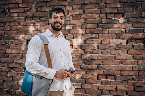 One man, portrait of a modern young businessman using smart phone while standing by a brick wall.