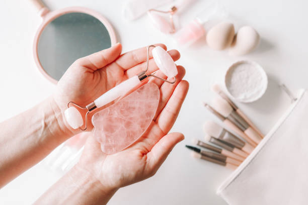 istock Woman holding gua sha tool and cosmetic over white table, top view 1432299791