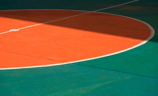 Sunlight and shadow on surface of orange circle center with white line on green concrete ground of outdoor futsal court