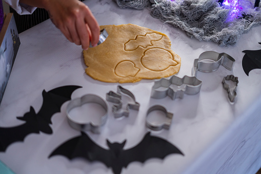 Latin woman of average age of 25 years old, a pastry chef by profession dressed in a black striped apron and white uniform is in the kitchen of her home preparing cookie dough with halloween molds