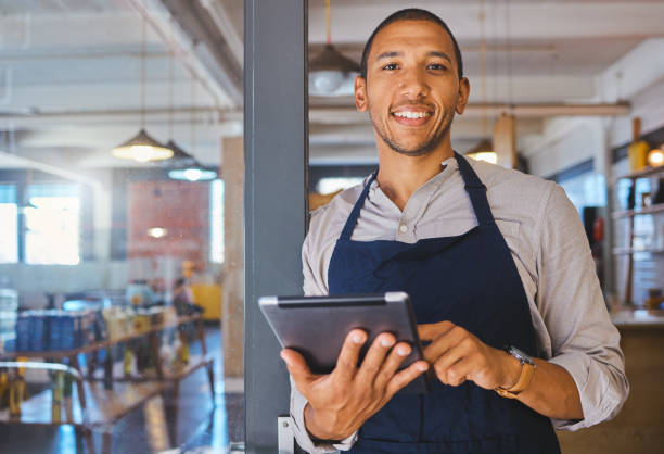 empreendedor de restaurante com tablet, apoiado na porta e aberto ao retrato dos clientes. proprietário, gerente ou funcionário de uma startup de fast food, café ou negócio de cafeterias felizes com um sorriso - bill looking cheerful latin american and hispanic ethnicity - fotografias e filmes do acervo