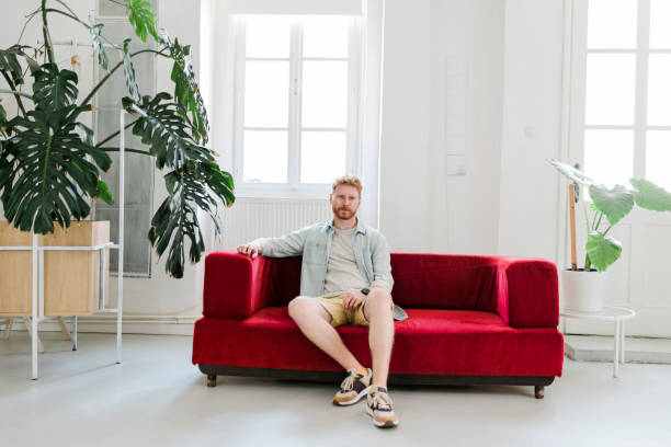 istock Serious man sitting on red sofa at home 1432312899