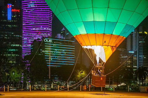 Singapore, Singapore - October 9, 2022: Staff from Ballons du Monde test the burner of a tethered hot air balloon at an open space in front of skyscrapers around Marina Bay at night.