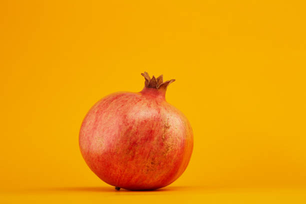 Ripe and juicy pomegranate fruit on orange background with soft shadow