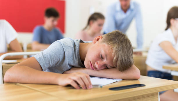 istock Bored teenage boy sleeping at desk in classroom during lesson 1432318962