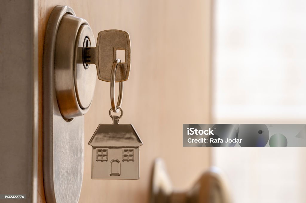 CLOSE UP OF KEY AND HOUSE KEYCHAIN ​​IN HIGH SECURITY DOOR LOCK. HOME INSURANCE CONCEPT. COPY SPACE. Residential Building Stock Photo