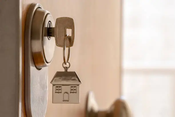 CLOSE UP OF KEY AND HOUSE KEYCHAIN ​​IN HIGH SECURITY DOOR LOCK. HOME INSURANCE CONCEPT. COPY SPACE.