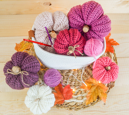 colorful woolen crochet pumpins in autumn in a white basket with lights, crochet hooks, autumn leaves and cozy atmosphere and woolen balls