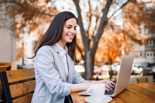 Young businesswoman sitting in a sideway cafe, drinking coffee working on laptop