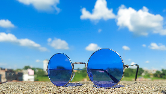 The round glass sunglass with the background of blue sky. The background of sky looks very beautiful. The sky looks bright and clear because of scorching sun and rain which happened two days ago. This sky is the indication of winter.