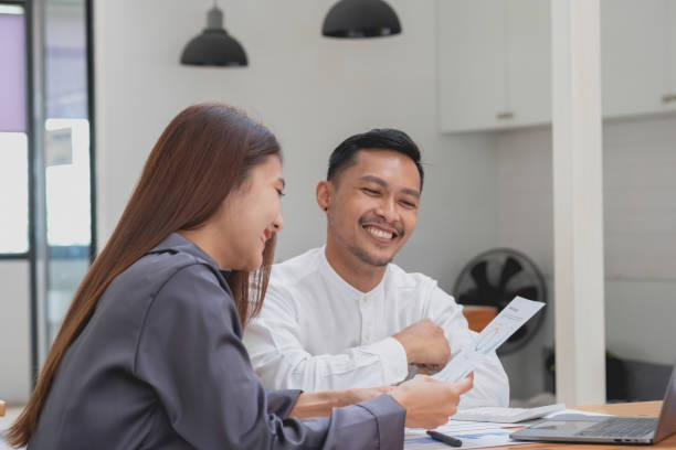 Two male and female marketers use company documents and use laptop computers to record data to analyze company profits.