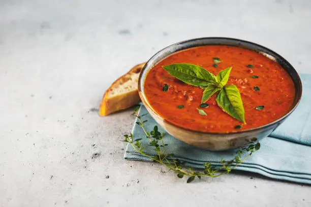 Bowl of fresh homemade tomato basil soup with fresh herbs and slice of focaccia bread with space for text