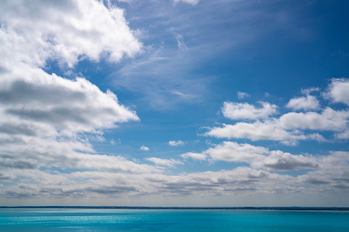 White cumulus clouds over sea horizon in a blue summer sky background