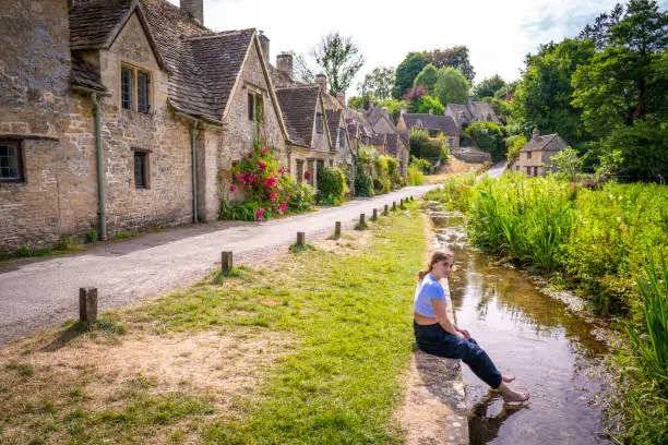 Bibury, young girl blond tourist student in Arlington Row in the England Cotswolds one of the most beautiful villages in the England countryside, UK