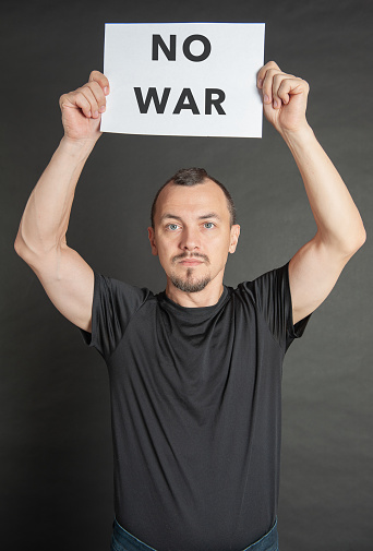 Young handsome man holds no war sign under his head on dark background