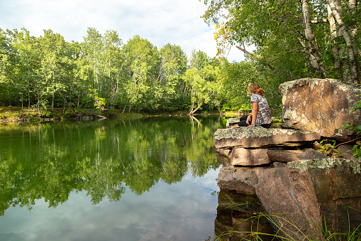 Girl sitting on a rocky ledge of an old quarry pond.