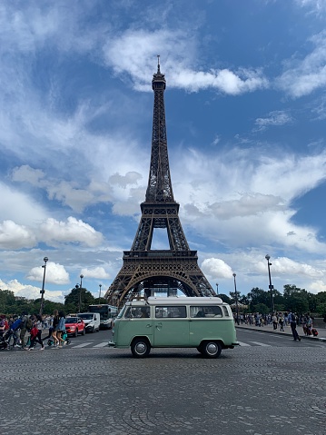 Old VW kombi campervan (1974) driving in front of the Eifel tower in Paris late in the afternoon in summer.