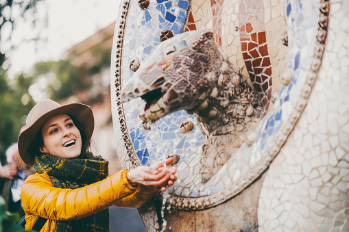 Smiling woman with hands cupped enjoying the running water of the Guell lizard