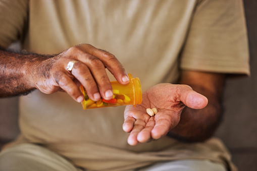 Medicine, healthcare and pills in the hands of a senior man sitting on a sofa in the retirement home. Prescription, medication and antibiotics for chronic treatment and wellness with a pensioner