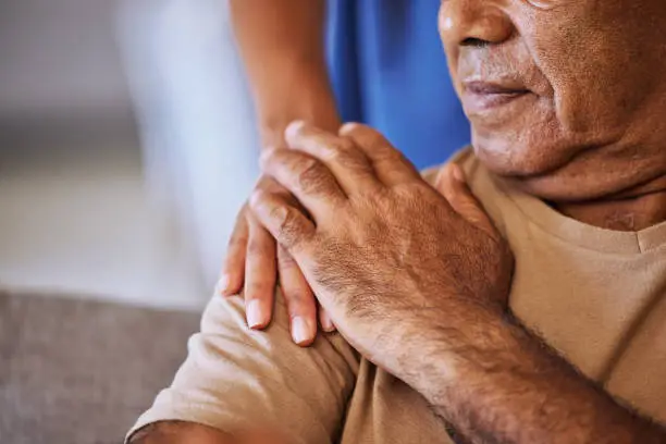 Photo of Support, care and helping hands for an elderly patient during a consultation at a nursing clinic. Closeup of hope, trust and comfort from a woman caregiver consulting a senior man in retirement home