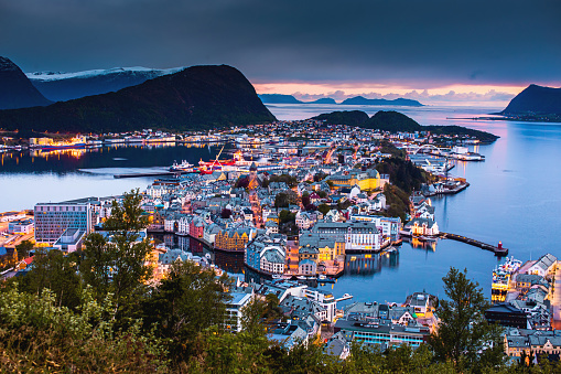 Evening photo of Alesund city in Norway. Beautiful night landscape with fjord. Scandinavia. Reflection of lamps on water. Twilight in mountains