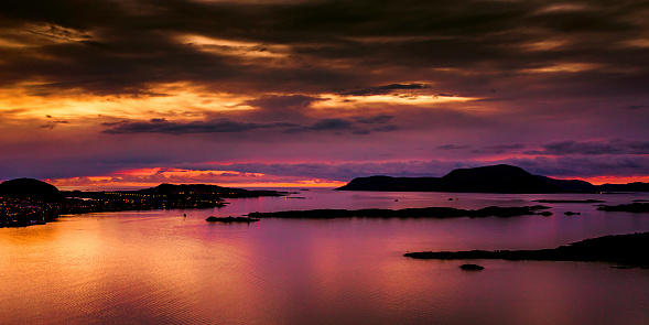 Evening photo of Alesund city in Norway. Beautiful night landscape with fjord. Scandinavia. Reflection of lamps on water. Twilight in mountains