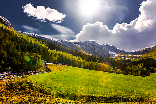 Green field. Picturesque sunny landscape in Norway. Snow on mountain. Spring. Beautiful north nature. Scandinavia. Adventure in mountains. Norwegian climate