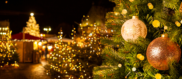 European Christmas city with festive fair or market in the evening. Christmas tree with beautiful balls on foreground. Holiday background.