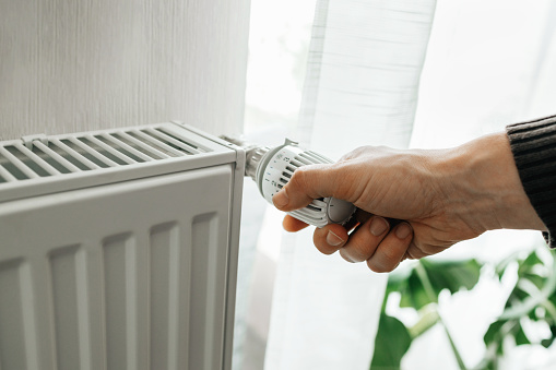 A man regulates the temperature on the radiator at home. Rising prices for heating in households. The concept of the energy crisis in Europe.