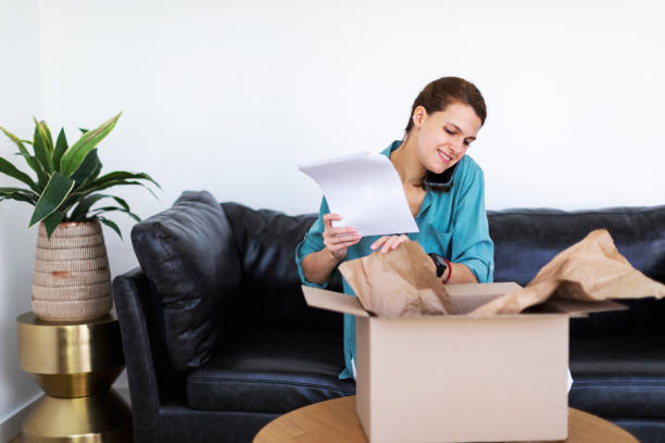 istock Young adult woman opening package with and using mobile 1432343363