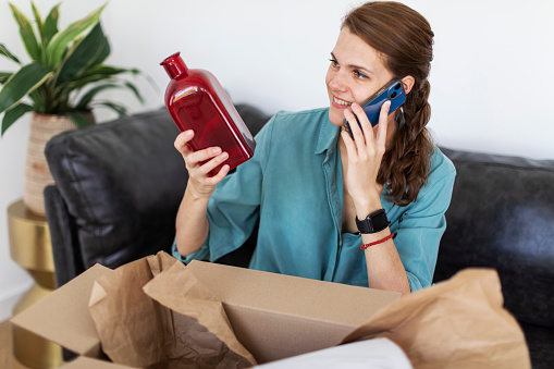 Young adult woman opening package with and using mobile
