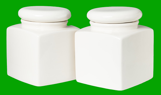 two white ceramic jars for food storage in the kitchen isolate on a green background.