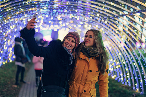 Mother and daughter taking selfies in a tunnel with Christmas lights in public park
Canon R5