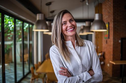 Portrait of a mature woman standing in her restaurant looking proudly and happily at the camera.