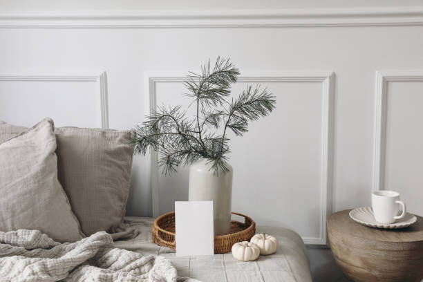 istock Empty Christmas greeting card, invitation mockup. Bed, sofa with linen cushions, blanket. Pine tree branches in vase. White little pumpkins on wicker tray, wooden coffe table with cup. Winter interior 1432350821