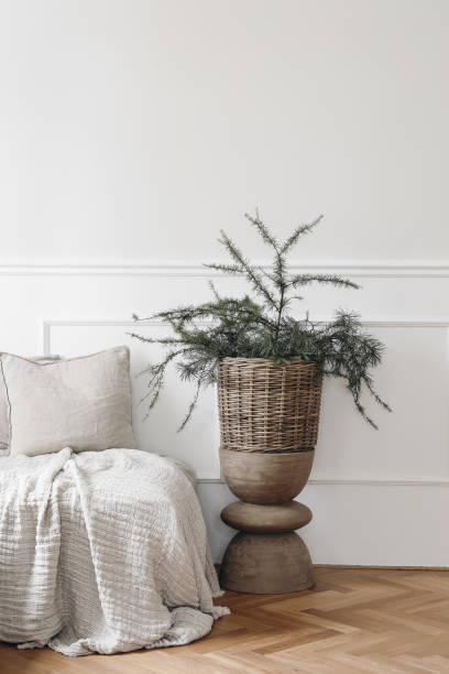 istock Elegant Christmas interior. White moulding panelling wall background, empty copy space. Bed, sofa with linen cushions, throw. Evergreen larch, pine tree branches in wicker basket, wooden coffee table. 1432350823