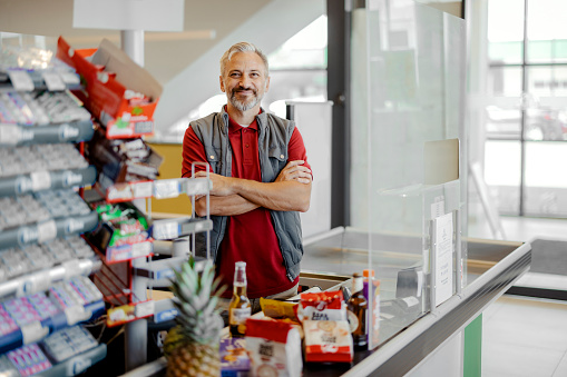 Portrait of mature adult male cashier looking at camera with crossed arms at supermarket
