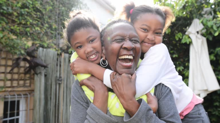 Laughing grandma and grandkids hugging outside in their yard