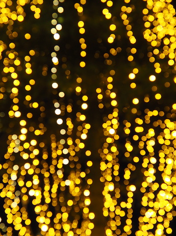 bokeh highlights. Golden and yellow color flashes in the dark. Festive background. Blurred defocus. Decoration of city streets. Many yellow balls. Many yellow, white and orange circles